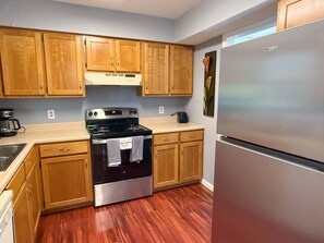 A kitchen with wooden cabinets, a stainless steel refrigerator, and a black stove. - 2BR Condo in Pointe Royale with View ~ 2 Pools ~ FREE TICKETS INCLUDED! (PR2-6) (Branson)