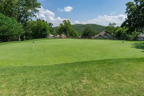 Ein Golfplatz mit einer Fahne, Bäumen und Gebäuden im Hintergrund.
