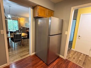 A kitchen with a refrigerator, wooden cabinets, a dining area with chairs, and a view of a balcony. - 2BR Condo in Pointe Royale with View ~ 2 Pools ~ FREE TICKETS INCLUDED! (PR2-6) (Branson)