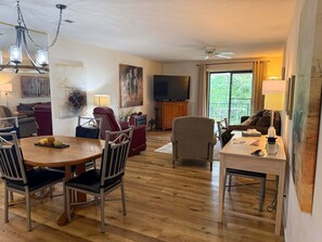 Ein geräumiger Wohnbereich mit Esstisch, Stühlen, einer Couch, einem Fernseher und einem Balkon mit Blick.