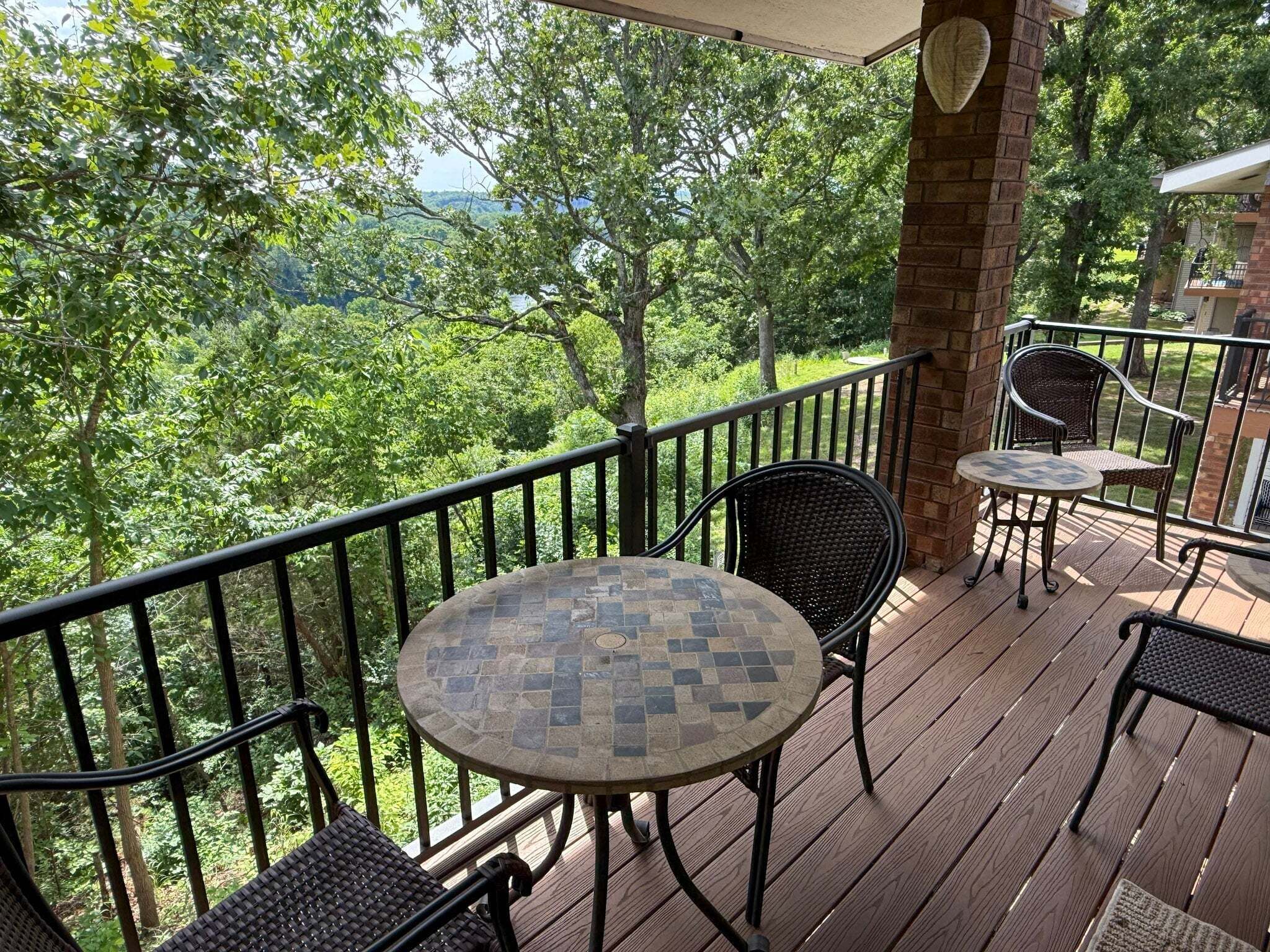 A wooden deck with a round table and chairs, a brick pillar, and a view of trees and hills.