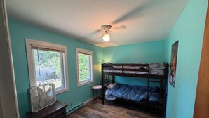 Una habitación con paredes verde azulado, una cama doble, un ventilador de techo y una ventana con vistas a la vegetación.