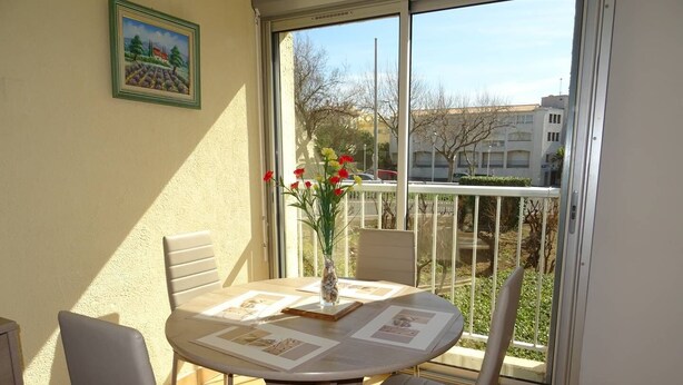 A balcony with a table, chairs, a vase with flowers, and a framed picture on the wall. - CAP D'AGDE - Plage du Môle / Réf 133 (CAP D'AGDE)