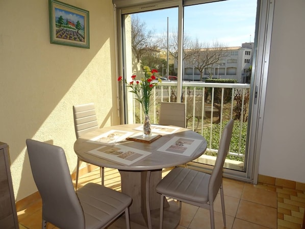 Ein Balkon mit Tisch, Stühlen, einer Blumenvase und einem gerahmten Bild an der Wand.