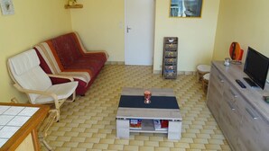 A living room with a sofa, a coffee table, a TV, a cabinet, and a door. - CAP D'AGDE - Plage du Môle / Réf 133 (CAP D'AGDE)