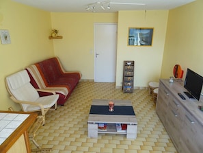 Ein Wohnzimmer mit Sofa, Couchtisch, Fernseher, Schrank und einer Tür.