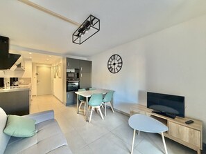 Ein modernes Wohnzimmer mit Essbereich, Fernseher und einer Küche im Hintergrund.