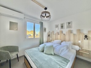 Ein Schlafzimmer mit einem Bett, einem Sessel, einem Fenster mit Blick und einer Wandleuchte.