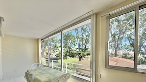 Ein Zimmer mit Tisch und Stühlen, großen Fenstern und Blick auf Bäume und Gebäude.