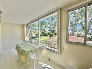 Ein Zimmer mit Tisch und Stühlen, großen Fenstern und Blick auf Bäume und Gebäude.