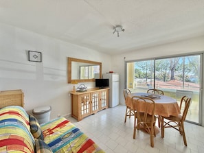 Ein Zimmer mit einer Couch, einem Esstisch mit Stühlen, einem Fernseher auf einem Schrank und einem großen Fenster mit Blick auf Bäume und Gebäude.