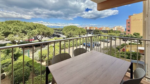 A balcony with a table and chairs, overlooking a parking area and buildings. - CAP D'AGDE - Plage du Môle / Réf 0101 (CAP D'AGDE)