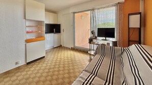 A hotel room with a bed, a desk with a computer, a TV, a kitchen area, and a balcony with a view. - CAP D'AGDE - Plage du Môle / Réf 0101 (CAP D'AGDE)
