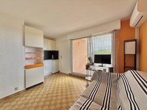 A hotel room with a bed, a desk with a computer, a TV, a kitchen area, and a balcony with a view. - CAP D'AGDE - Plage du Môle / Réf 0101 (CAP D'AGDE)