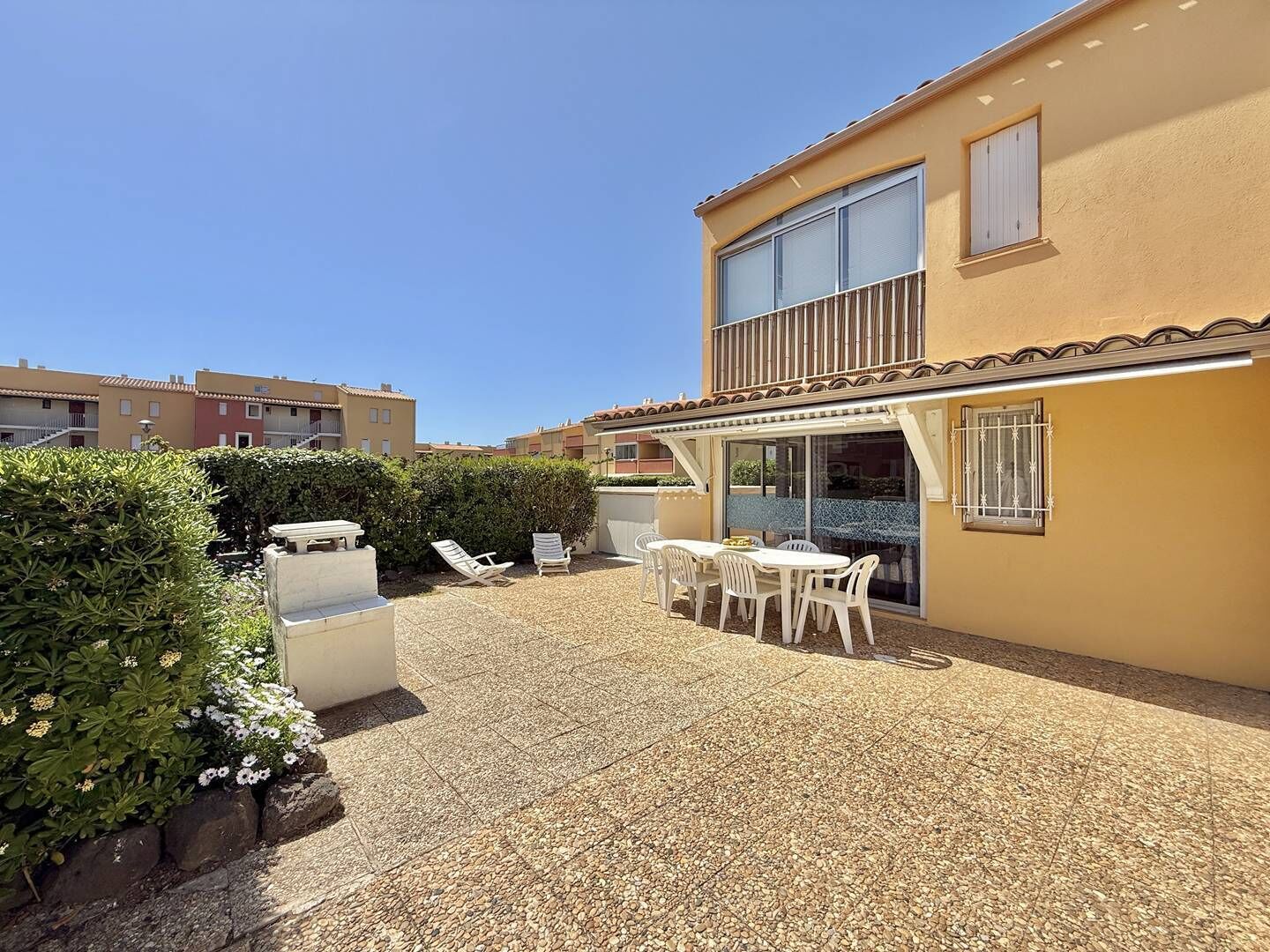 A residential building with a patio area featuring a table and chairs, a covered seating area, and a view of neighboring buildings.
