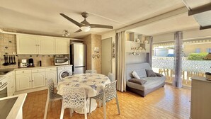 A compact kitchen with white cabinets, a microwave, and a refrigerator. There is a dining area with a table and chairs, and a sofa in the living area. - CAP D'AGDE - Plage Richelieu // Réf 0157 (CAP D'AGDE)