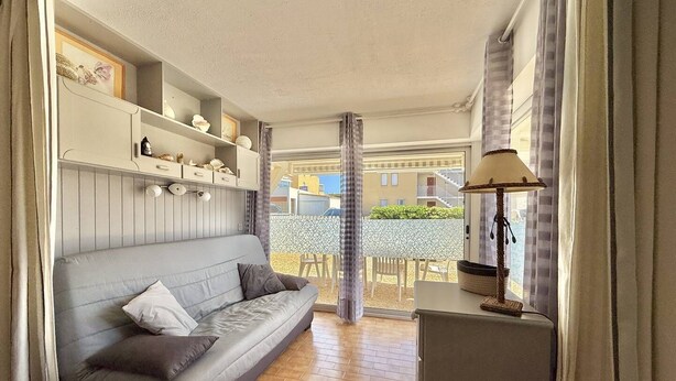A living room with a sofa, a lamp, and a view of the outside. - CAP D'AGDE - Plage Richelieu // Réf 0157 (CAP D'AGDE)