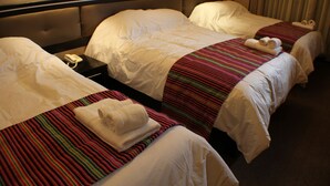 Quarto de hotel com três camas, cada uma com manta listrada e toalhas dobradas.