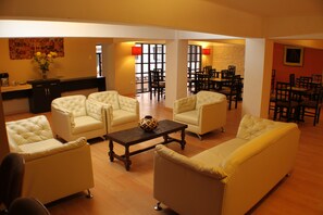 A spacious living area with a sofa set, a coffee table, and a dining area with chairs and tables. - Triple Room - Tampu Hotel. (Cusco)