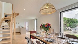 A modern dining area with a wooden staircase, a large window, and a hanging light fixture. - Maguyann - PLOUHARNEL (PLOUHARNEL)