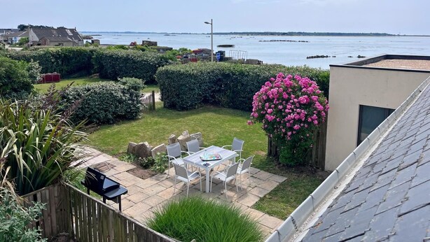 A residential backyard with a patio, a table, and chairs, a pink flowering bush, and a view of the sea. - Maguyann - PLOUHARNEL (PLOUHARNEL)