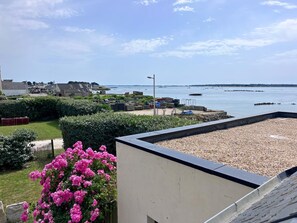 A coastal view with a pebbled beach, a garden with pink flowers, and a clear sky. - Maguyann - PLOUHARNEL (PLOUHARNEL)