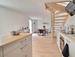 A modern kitchen with wooden countertops, a dining area with a table and chairs, and a staircase leading to an upper level. - Maguyann - PLOUHARNEL (PLOUHARNEL)