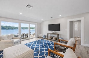 Un salon spacieux doté d’une grande fenêtre donnant sur un lac, d’un téléviseur à écran plat fixé au mur et d’un coin salon confortable agrémenté d’un tapis à motifs.