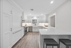 Une cuisine moderne avec des meubles blancs, un îlot central et une grande fenêtre.