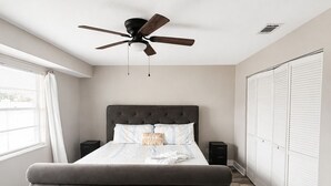 Un dormitorio con una cama con cabecera capitonada, ventilador de techo, ventana con persianas y armario con puertas correderas.