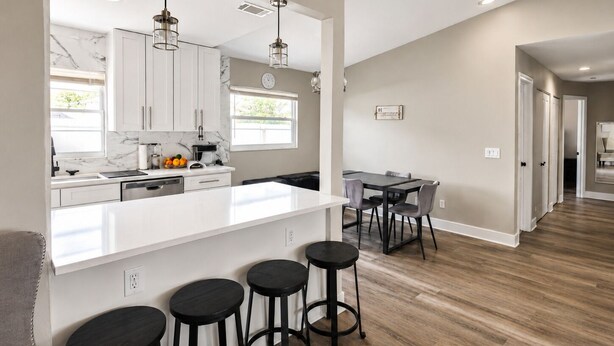 Una cocina moderna con armarios blancos, salpicadero de mármol y una isla central con taburetes.