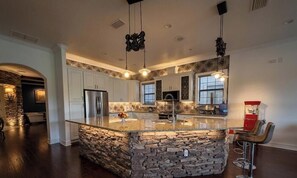 Una cocina con isla de piedra, armarios blancos e iluminación colgante.