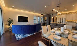 Una sala de estar moderna con un sofá azul, una mesa de comedor con platos, y una cocina al fondo.