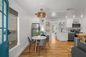 Une cuisine moderne avec des meubles blancs, un îlot central et un coin repas comprenant une table ronde et des chaises.