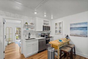 A modern kitchen with white cabinetry, stainless steel appliances, and a wooden dining table with bar stools. - Hot TUB! MIN to Beach! JUST Remodeled. Lux 1/1 Free Parking. Pet Friendly. (Galveston)