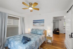 Ein Schlafzimmer mit Bett, Deckenventilator, einem Gemälde und Blick in einen weiteren Raum.
