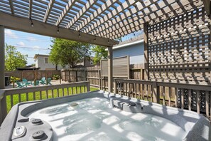 Un bain à remous sous une pergola, avec une clôture en bois et des chaises en arrière-plan.