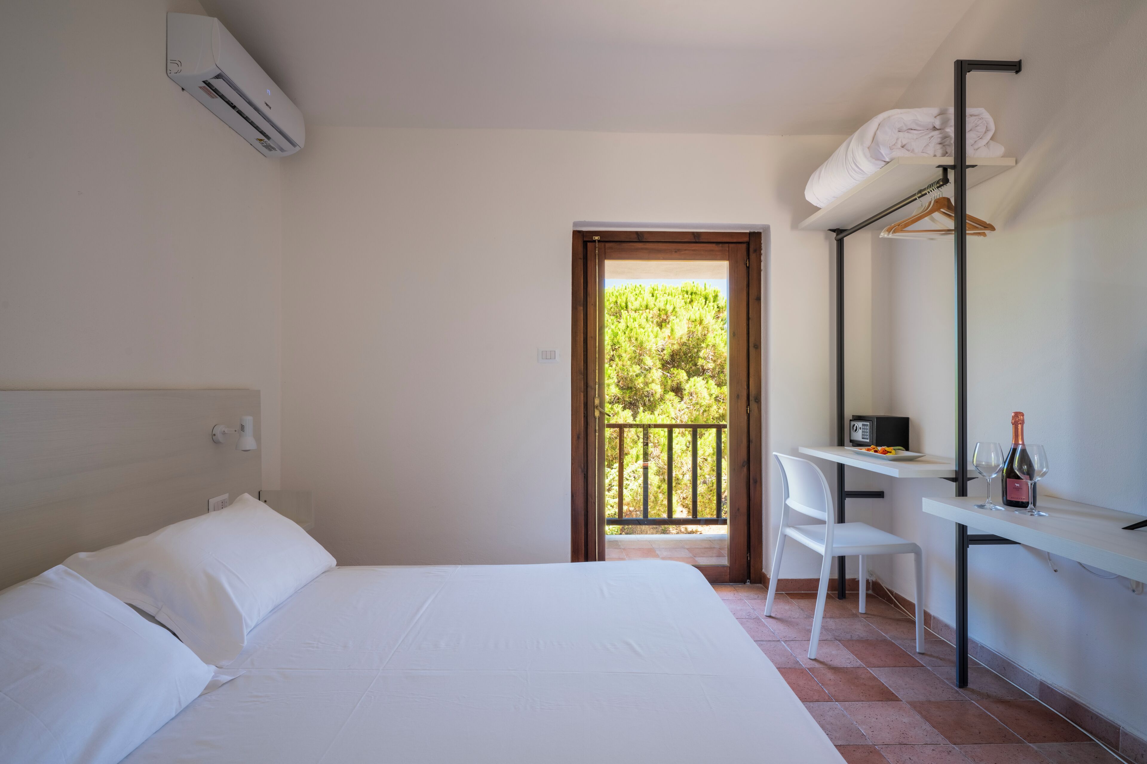 Habitación de hotel con cama, escritorio, silla, balcón y unidad de aire acondicionado.