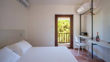 Habitación de hotel con cama, escritorio, silla, balcón y unidad de aire acondicionado.
