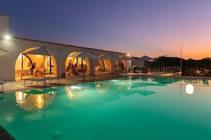 A swimming pool with lounge chairs and umbrellas, surrounded by a building with arched openings. - Q Resort Hotel (Sorso)