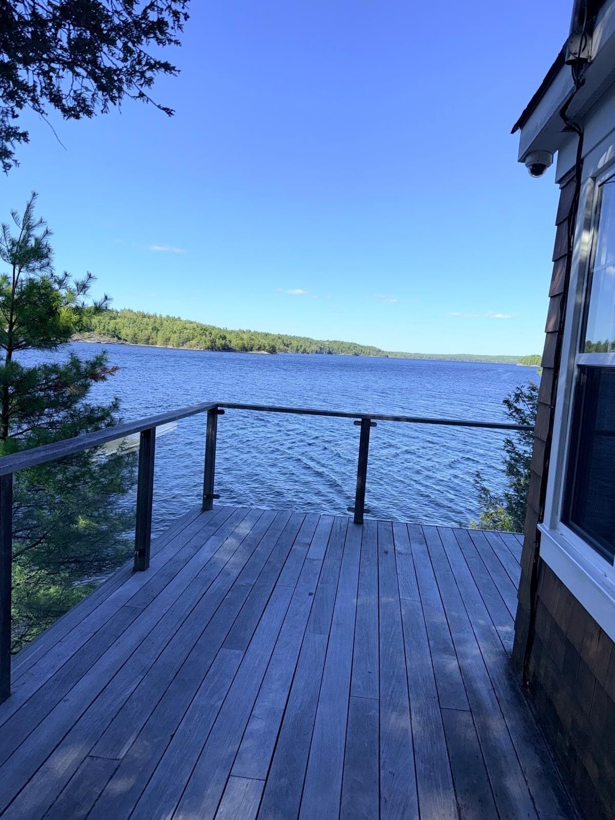 Eine Holzterrasse mit Geländer, die auf einen See mit umliegenden Bäumen blickt.