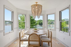 Ein Esszimmer mit rundem Tisch, vier Stühlen, einer Deckenleuchte und großen Fenstern mit Blick auf einen See und Bäume.