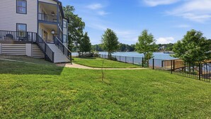 A two-story building with a balcony, a grassy yard, and a lake view. - Casa del Sol | Pickle ball court| Fire pit | Dock | Sleeps 10 (Mooresville)