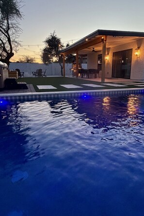 A swimming pool with a covered patio area, outdoor furniture, and a view of the house.
