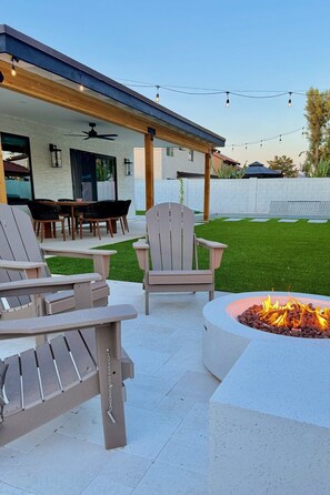 An outdoor patio with Adirondack chairs, a fire pit, and a covered seating area with a ceiling fan.