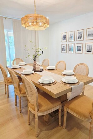 Ein Esszimmer mit einem Holztisch, gedeckt für sechs Personen, umgeben von sechs Stühlen, einer Hängeleuchte und gerahmten Bildern an der Wand.