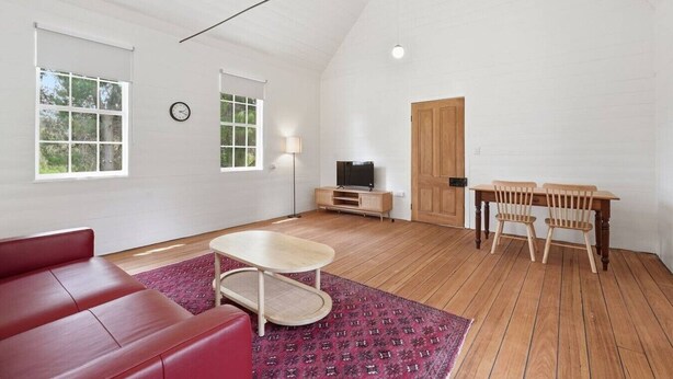 Une pièce spacieuse avec un canapé rouge, une table en bois et un téléviseur posé sur un meuble en bois.