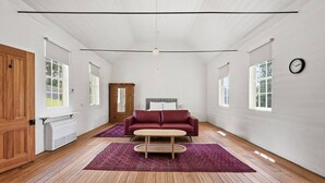 Une pièce spacieuse dotée d’un plancher en bois, d’un canapé rouge, d’une petite table ronde et d’une grande fenêtre laissant entrer la lumière naturelle.
