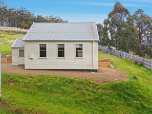A single-story house with a metal roof, a fenced yard, and a grassy area in front. - Restored 1881 church for two, valley views, 30 minutes from Hobart (Collinsvale)