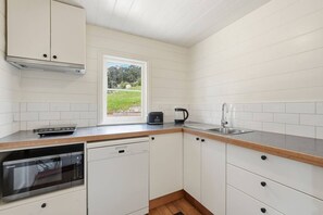 A kitchen with white cabinets, a stainless steel sink, a microwave, and a window with a view of greenery. - Converted Church Escape (Collinsvale)